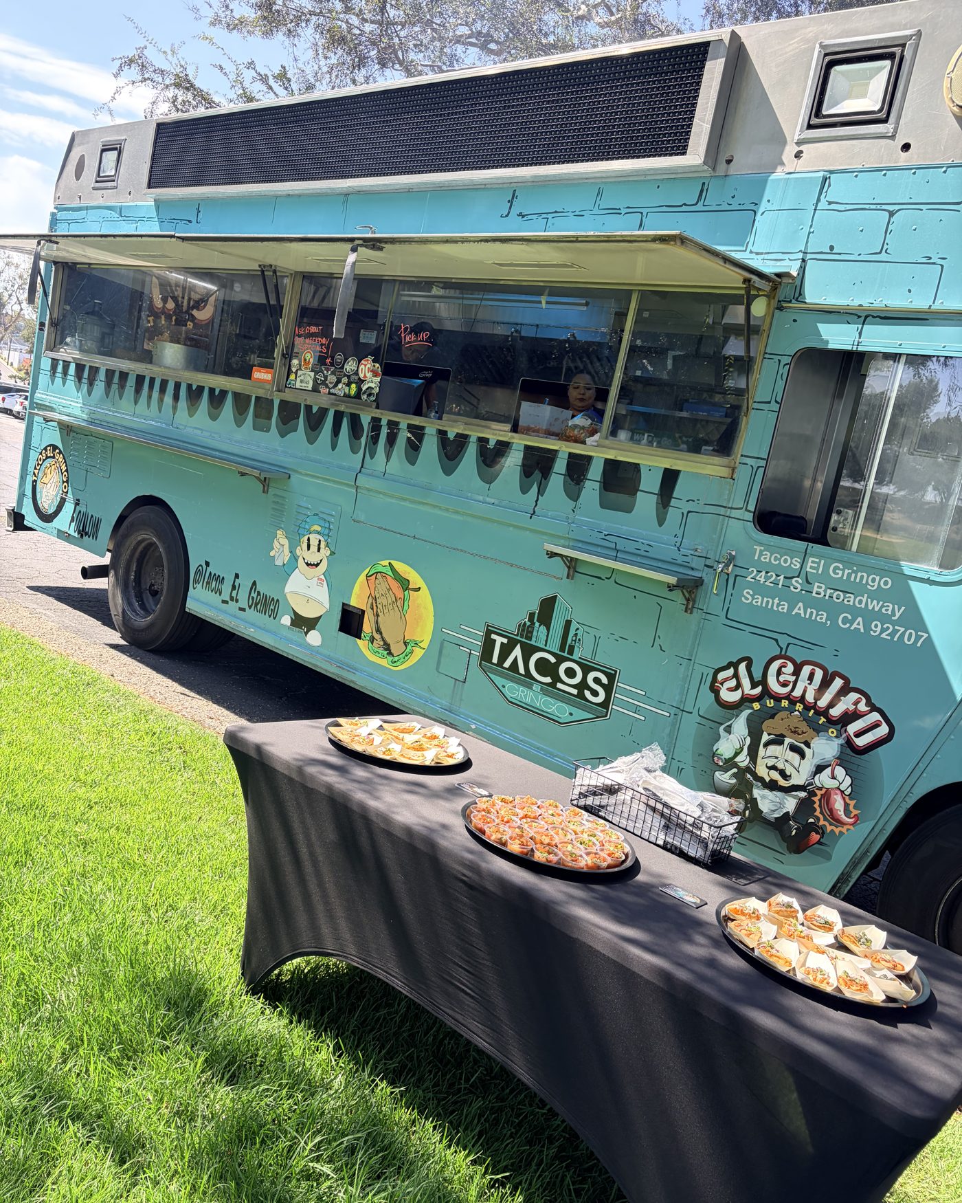 El truck en un evento con mesa de comida sobre el pasto